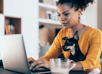 Young self-employed woman working on her laptop at home with her small dog sitting with her