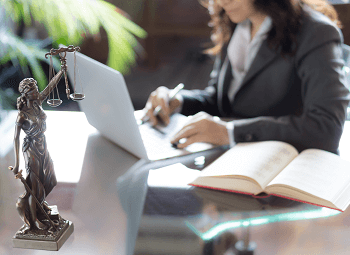 Woman working on a laptop with a small statue of lady justice holding her scales up on her desk