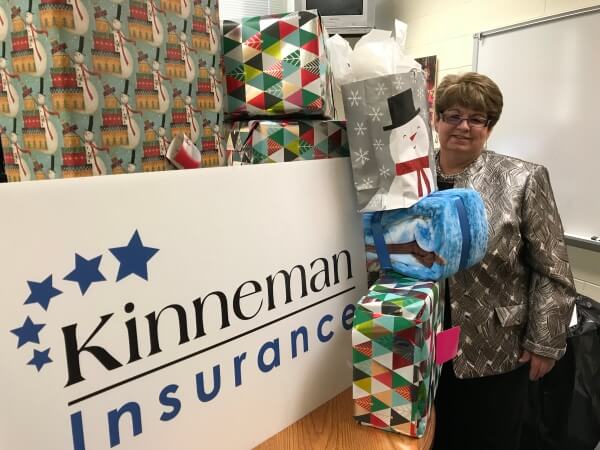 Virginia Kinneman beside a Kinneman Insurance sign and several wrapped presents