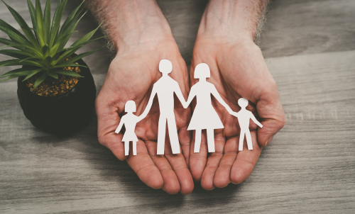 person cupping paper cutout of family in hands