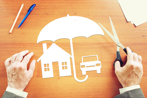 person holding scissors, paper cutout of umbrella, house and car on table